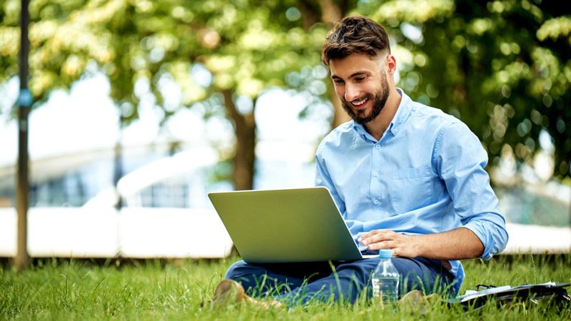 Happy teacher sitting outside on a sunny day, using a laptop to generate lesson plans with Kangaroos AI lesson plan generator software, smiling contentedly, illustrating time-saving technology in education