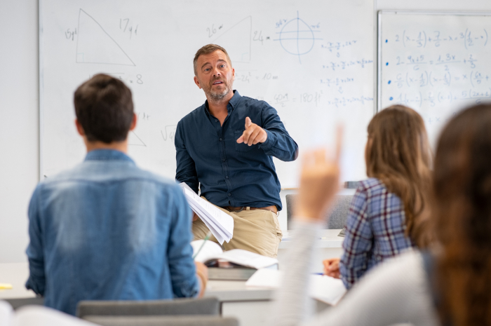 A teacher uses a structured rubric generated by an AI tool to instruct attentive students in a well-equipped classroom, indicating an interactive and technology-integrated learning environment.